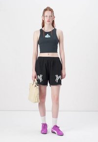 Shorts noirs avec un motif animal blanc et des bordures, associés à un crop top sombre avec un logo bleu clair. Les accessoires comprennent un sac en toile beige.
