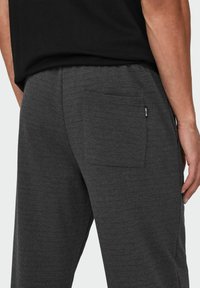 Donkergrijze sweatpants van zacht materiaal, met een enkele achterzak en een elastische tailleband voor extra comfort. Textuurdetails zijn zichtbaar.