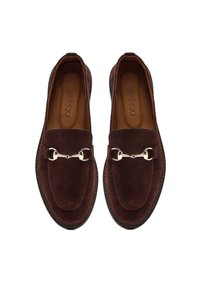 Un paio di mocassini in suede marrone con dettaglio in metallo a forma di morso d'oro e soletta in pelle, visti dall'alto su sfondo bianco.
