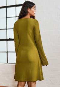 Langärmliges, geripptes Kleid in Olivgrün mit einem Schiffsaugen-Ausschnitt und einem ausgestellten Saum, aus einem strukturierten Stoff gefertigt.