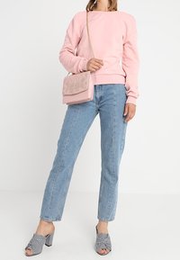Donna che indossa una felpa rosa, jeans azzurri chiari, sandali con tacco a strisce bianche e nere, e una borsa a spalla rosa con dettagli in perline.