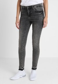 Jeans ajustados en denim negro desgastado con una textura suave, con una cintura alta, bolsillos delanteros y dobladillo deshilachado, combinados con zapatillas blancas.