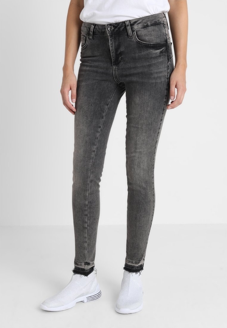 Jeans ajustados en denim negro desgastado con una textura suave, con una cintura alta, bolsillos delanteros y dobladillo deshilachado, combinados con zapatillas blancas.