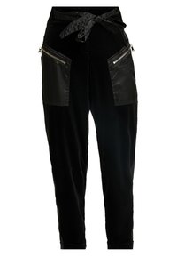Pantalons noirs fuselés avec ceinture en tissu nouée à la taille et grandes poches avant zippées avec garniture brillante.