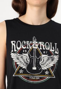 Juoda berankovė marškinėliai su grafiniu dizainu, kuriame tekstas "ROCK & ROLL", gitara, sparnai ir apvalūs akcentai raudonos ir žalios spalvų.