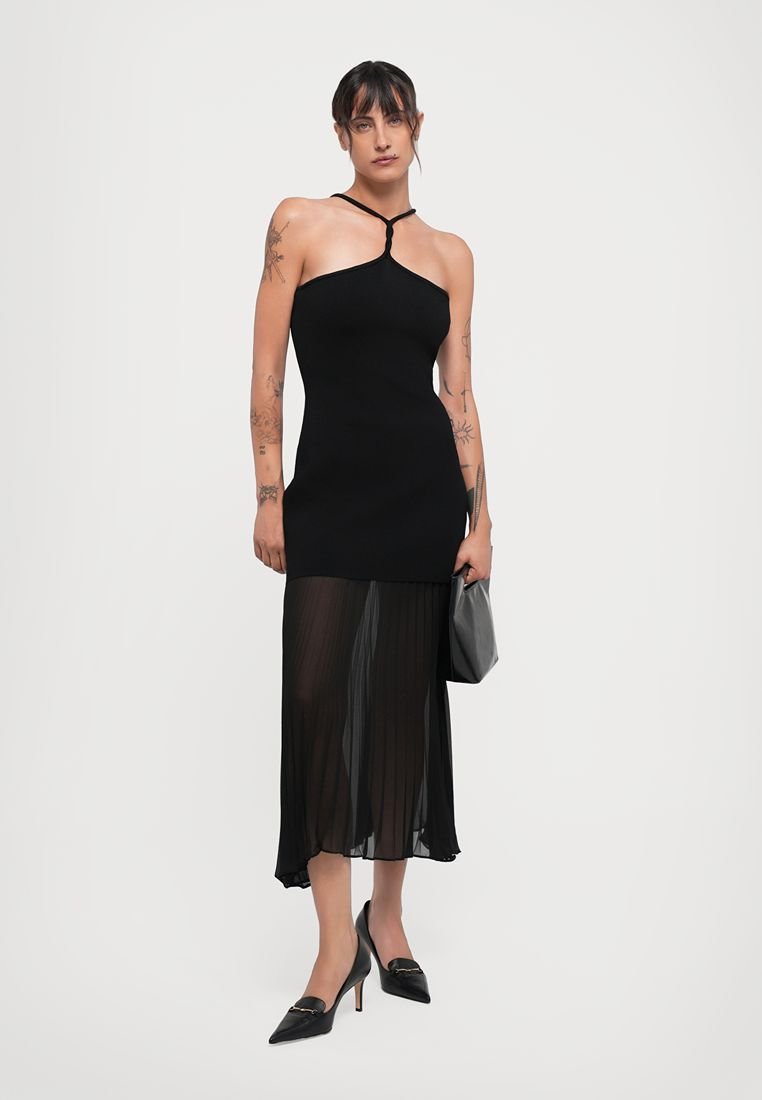 Robe noire avec un haut ajusté, des bretelles fines et une partie inférieure fluide et plissée. Portée avec des escarpins noirs à talons pointus et un sac assorti.
