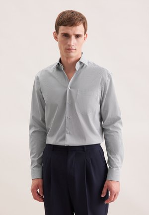 Camicia blu chiara con motivo, colletto standard, maniche lunghe e taschino sul petto, abbinata a pantaloni scuri. Dettaglio della trama del tessuto visibile.