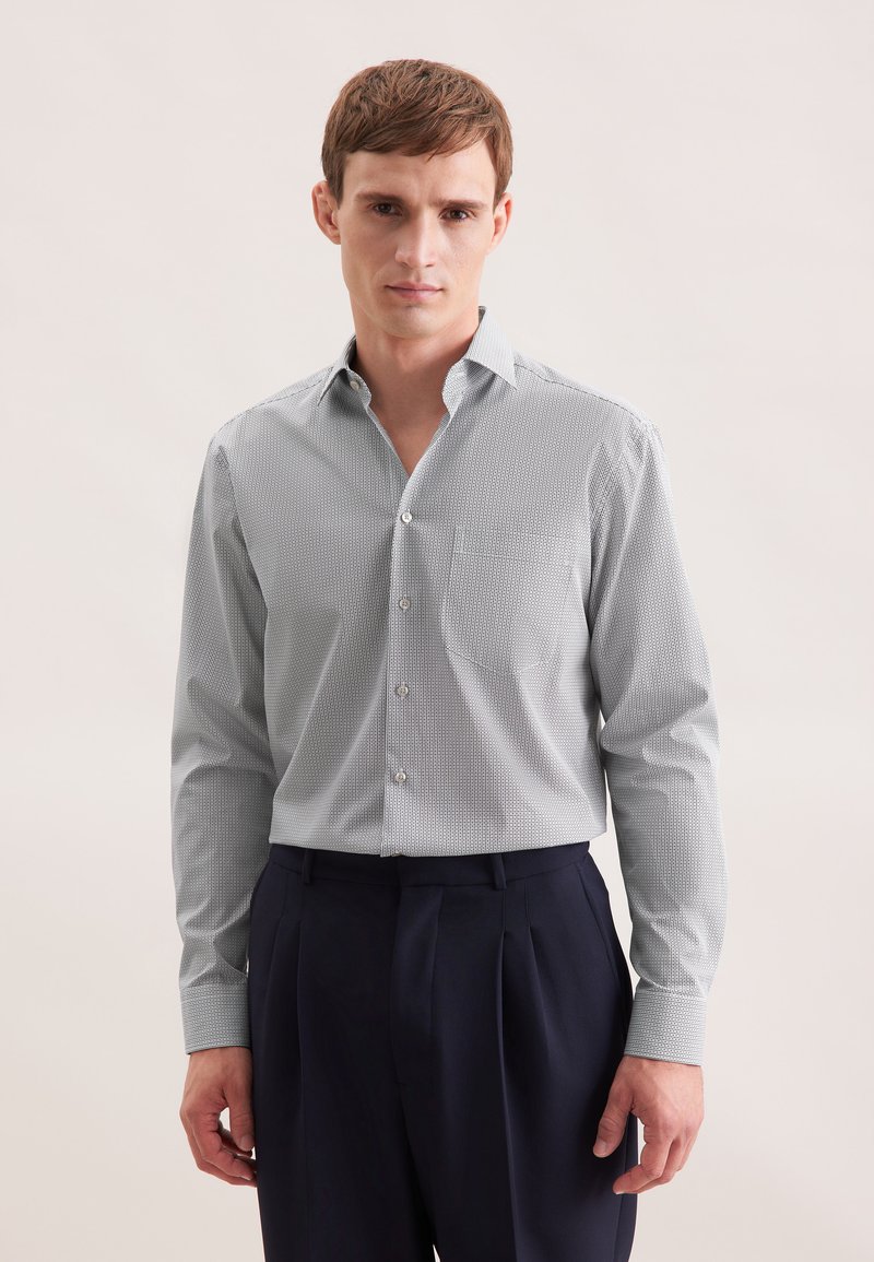 Camicia blu chiara con motivo, colletto standard, maniche lunghe e taschino sul petto, abbinata a pantaloni scuri. Dettaglio della trama del tessuto visibile.