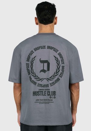 Graues, übergroßes T-Shirt aus Baumwolle mit einem großen bedruckten Design auf der Rückseite, das Text und ein rundes grafisches Motiv zeigt.