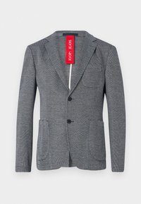 Γκρι ριγέ σακάκι με ραμμένα πέτα, δύο μπροστινές τσέπες και τρία κουμπιά. Κόκκινη ετικέτα μάρκας προσαρτημένη στο γιακά.