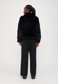 Μαύρο σακάκι από συνθετική γούνα με ψηλό κολάρο και χαλαρή γραμμή, με υφασμάτινα μανίκια. Συνδυάζεται με φαρδιές μαύρες παντελόνες και χοντρές μπότες.