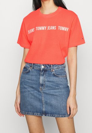 Jasnoczerwony T-shirt z napisem "JEANS TOMMY" w kolorze białym, zestawiony z niebieską dżinsową mini spódnicą z przodu zapinaną na guziki oraz kieszeniami.
