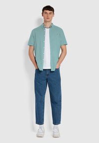 Mintgroene korteblouse shirt over een witte T-shirt, gecombineerd met losse blauwe jeans en witte sneakers. Minimalistisch ontwerp, geen patronen.