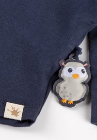 Navy blue cotton shirt with a textured fabric; features a playful owl-shaped tag with colorful accents and a small label at the hem.