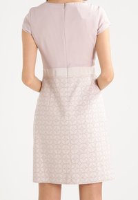 Robe à manches courtes en tissu rose pâle avec une partie inférieure à motif. Le dos comprend une fermeture éclair discrète et une ceinture unie.