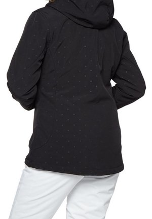 Persona con chaqueta negra con capucha con un sutil patrón de puntos, combinada con pantalones blancos, vista desde atrás.