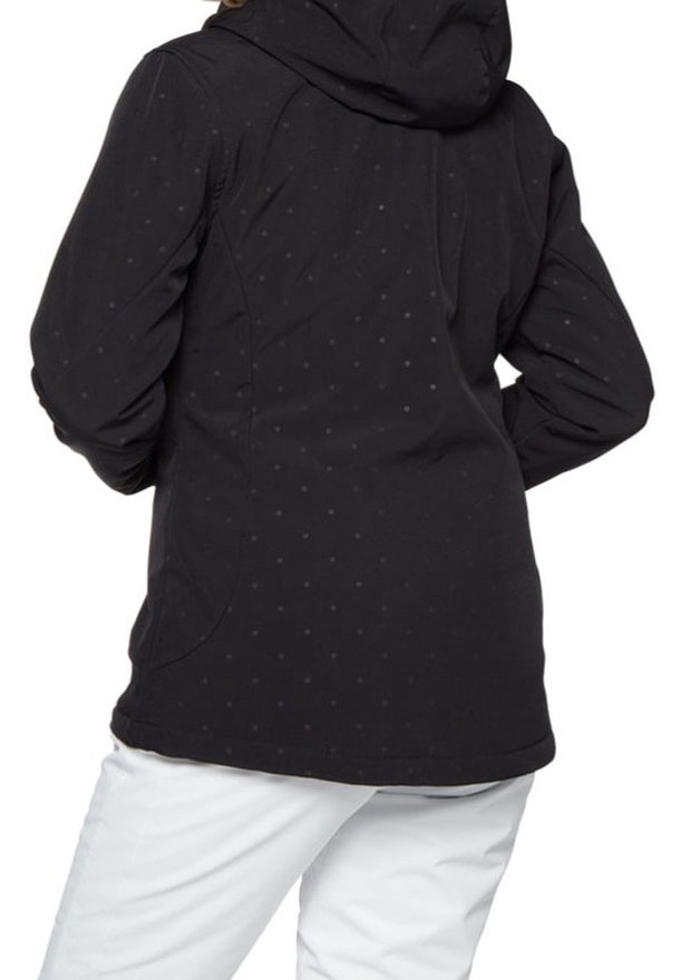 Personne portant une veste à capuche noire avec un motif discret de points, associée à un pantalon blanc, vue de dos.