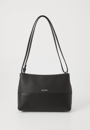 Musta Calvin Klein -laukkua, jossa on kaksi olkahihnaa, sileä yläosa, teksturoitu alaosa ja keskellä logo edessä.