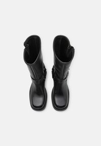 Botas de cuero negras con una textura suave, de altura hasta la mitad de la pantorrilla y dos correas ajustables a los lados, con un diseño de punta redonda.