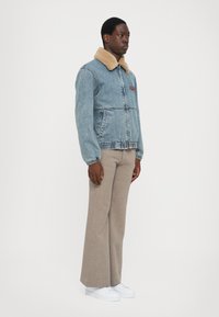 Denimjakk beezhi vale nahanaha, esipockets, elastne vöökoht; kantud beežide ruuduliste pükstega ja valgete tossudega.