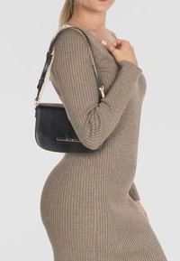 Borsa a tracolla in pelle nera con forma rettangolare, caratterizzata da una tracolla a catena con dettagli dorati e una superficie liscia, indossata su un outfit grigio.