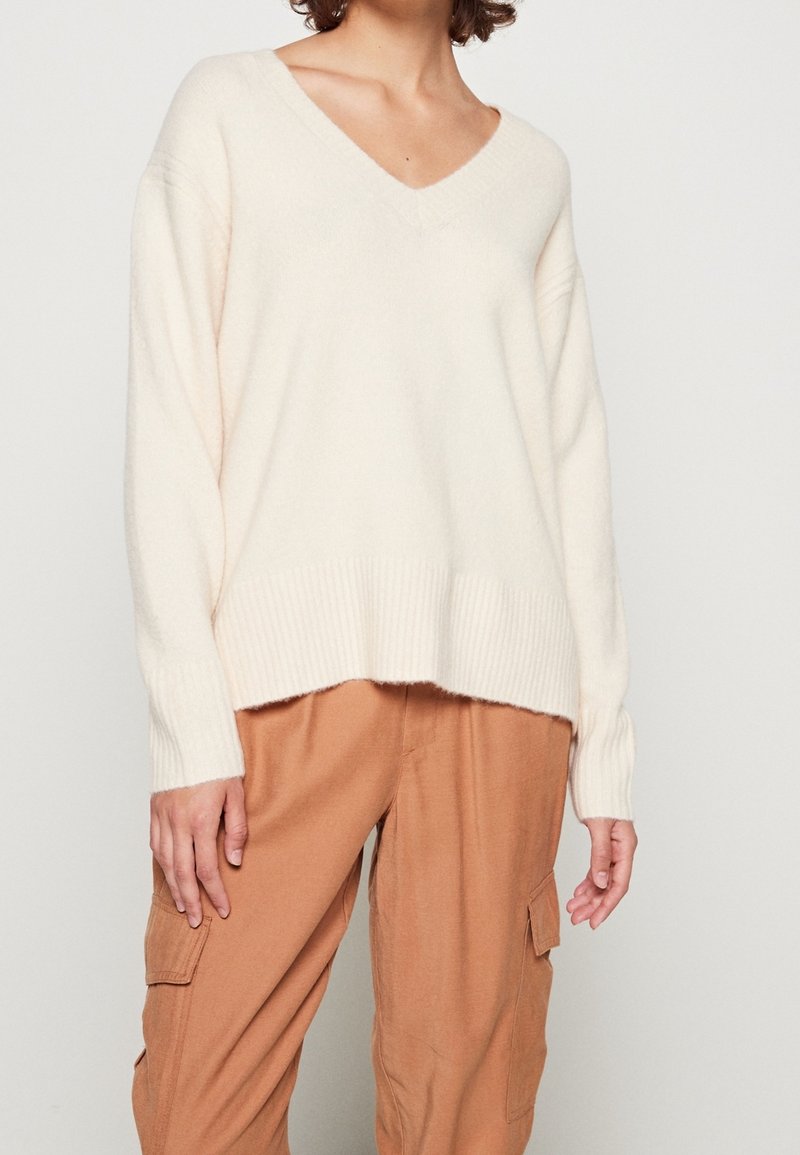 Maglione crema con scollo a V, spalle a coste e fondo a coste, texture morbida, vestibilità ampia, abbinato a pantaloni cargo beige con tasche laterali.