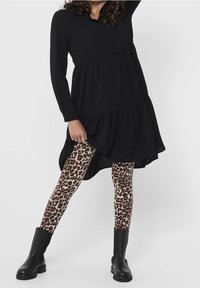 Abito nero a maniche lunghe con volant, abbinato a leggings leopardati marroni e neri e stivaletti neri.