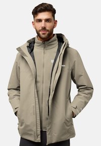 Giacca impermeabile beige con cappuccio e chiusura con zip, indossata sopra una giacca interna in pile grigia. Presenta un logo e tasche.