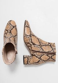 Botas tobilleras con un patrón de serpiente en tonos beige y marrón, que presentan una cremallera lateral, una superficie texturizada y un tacón grueso negro.