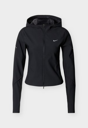 Melna sieviešu pieguļošā jaka ar rāvējslēdzēju, kapuci, garām piedurknēm ar caurumiem īkšķiem un mazs atstarojošs Nike logotips uz krūtīm un piedurknēm.