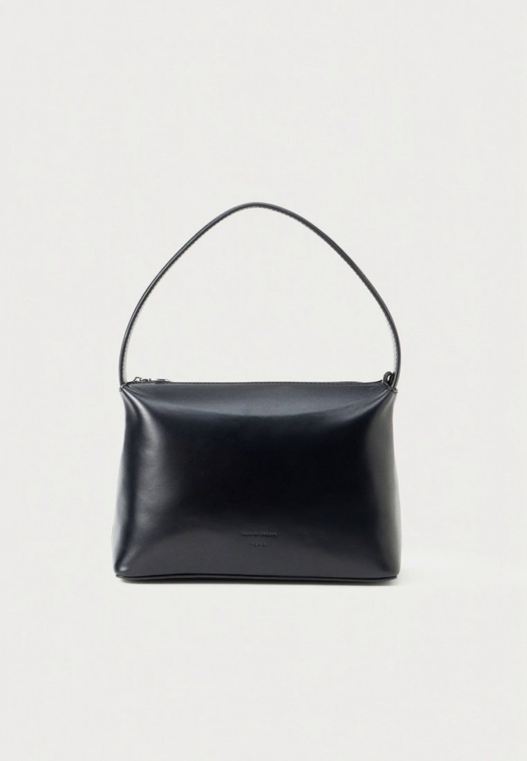Sac à main en cuir noir à texture lisse, fermeture zippée et une seule anse incurvée. Design minimaliste avec un branding subtil sur le devant.