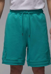 Turkise svedshorts med elastisk talje, snøre og sidelommer, der har en struktureret finish og unikke panel-syningsdetaljer.
