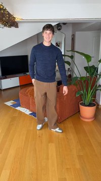 Tamsiai mėlynas megztinis su reljefinėmis juostomis, rudos plačios kelnytės ir sidabrinės avalynės. Vidaus apstatymas su vazoniniu augalu ir medinėmis grindimis.