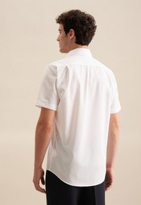 Camicia bianca a maniche corte con colletto a punta, tessuto liscio e orlo curvo. Design minimalista senza motivi o hardware visibile.