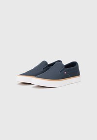 Mornarske slip-on cipele s rebrastom teksturom, s bijelim đonom i svijetlosmeđim naglaskom duž ruba đona. Bez vezica ili kopčanja.