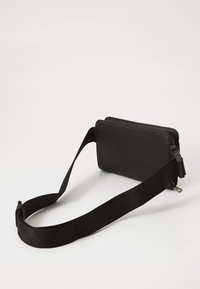 Čierna textúrovaná obdlžniková crossbody taška so širokým nastaviteľným popruhom a zipsovým uzáverom na bielom pozadí.
