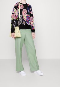 Pull tricot coloré avec une base noire et des motifs floraux, associé à un pantalon taille haute vert menthe et un sac à main jaune texturé.
