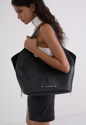 Black leather tote bag with a smooth finish, featuring silver hardware, a zip pocket, and a logo plate on the front.