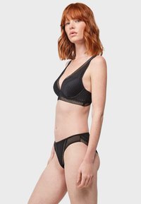 Set di reggiseno e perizoma neri con motivi testurizzati, dettagli in rete liscia e scollatura profonda, progettato per una silhouette aderente.