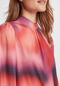 Flöjblus i rosa och lila gradient, med hög krage och puffärmar. Slätt tyg med mjuk lyster och subtila plisseringsdetaljer.