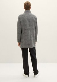 Dopasowany płaszcz w szaro-czarną kratę z wysokim kołnierzem, prostym krojem i dwoma tylnymi rozcięciami. W zestawieniu z ciemnymi spodniami i białymi trampkami.