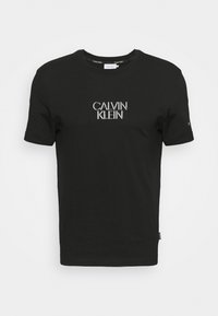 Camiseta de algodón negra con cuello redondo y mangas cortas, con "CALVIN KLEIN" impreso en plata en el pecho.