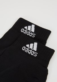 Calcetines de algodón negros con puños acanalados y logotipo de Adidas en blanco que presenta tres rayas. Textura suave y diseño de longitud hasta el tobillo.