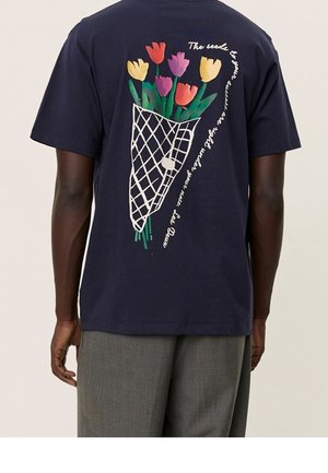 Osoba ubrana w granatową koszulę z kolorową grafiką bukietu tulipanów i kursywym napisem na plecach, w połączeniu z szarymi spodniami.