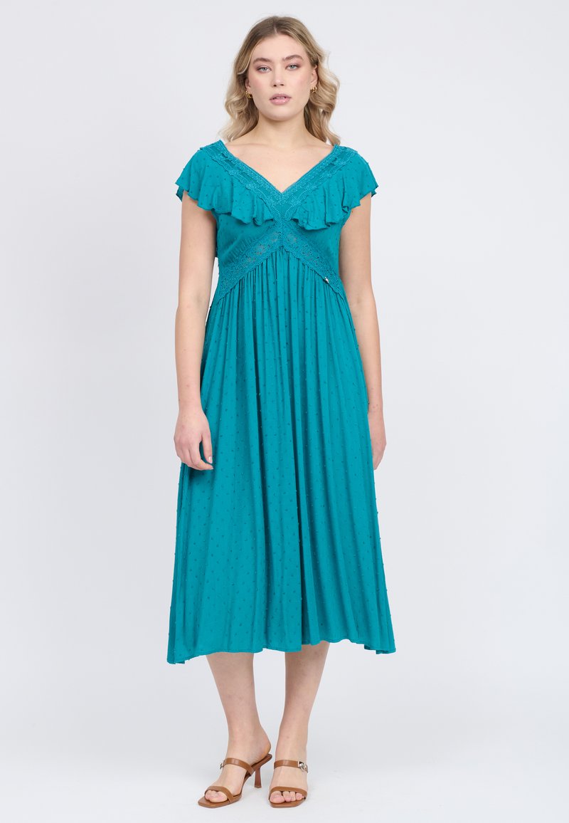 Vestido turquesa con mangas cortas con volantes, escote en V y un corpiño ajustado. La falda cae hasta la mitad de la pantorrilla con patrones de lunares texturizados.