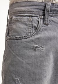Jeans de denim gris con un aspecto desgastado, con desgarros visibles, herrajes en tono plateado y un diseño clásico de cinco bolsillos.