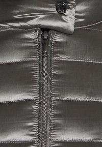 Grå dunjakke med en glat, skinnende finish. Har en central lynlås, trykknaplukning og vandret quiltet mønster.