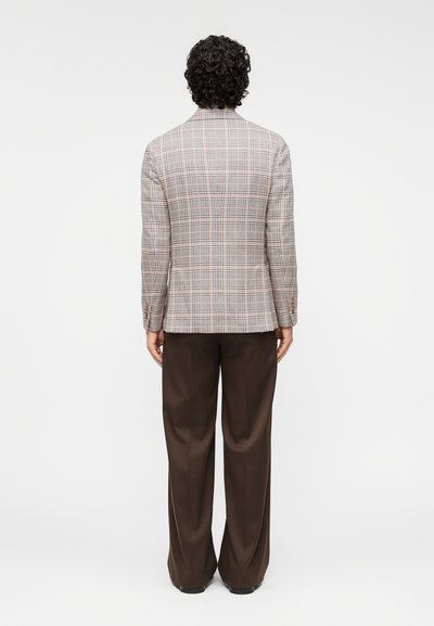Καφέ καρό σακάκι με δομημένη γραμμή, μονό άνοιγμα πίσω και αντίθετα κουμπιά. Συνδυασμένο με χαλαρά σκούρα καφέ παντελόνια.