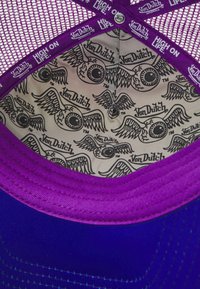 Ljubičasta i plava kapa s mrežastim dizajnom. Unutrašnjost sadrži uzorak krilatih očiju u crnoj boji na bež pozadini, s etiketom marke.