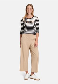 Gestreiftes Schwarz-Weiß Langarmshirt mit "SMILE" Druck, kombiniert mit beigen, weit geschnittenen Hosen und weißen Sneakers mit tanfarbenen Akzenten.